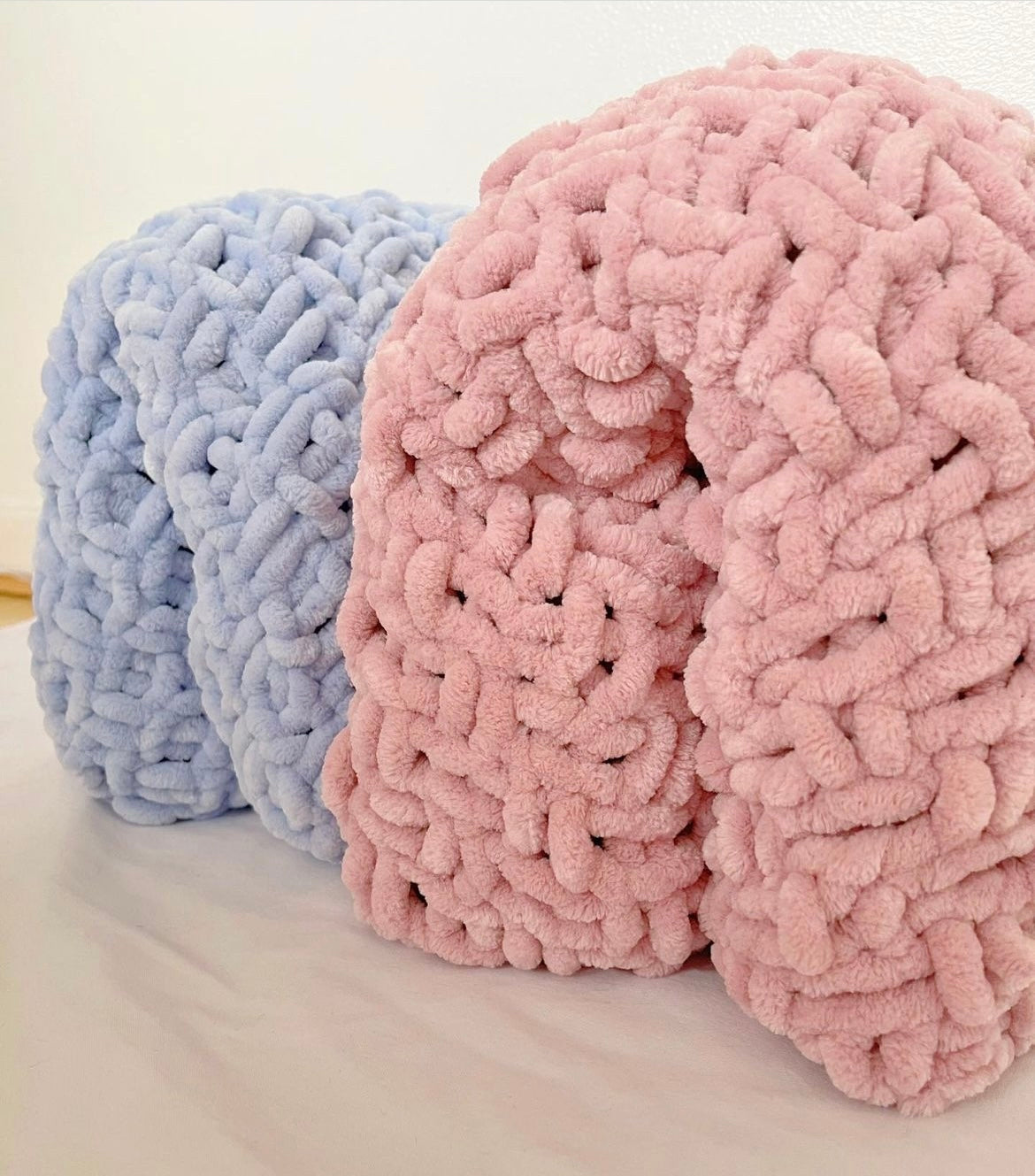 Two hand-knitted chenille toddler blankets in dusky pink and blue, rolled and displayed side by side, showcasing thick, ultra-soft texture—perfect for cosy toddler bedding or nursery decor.