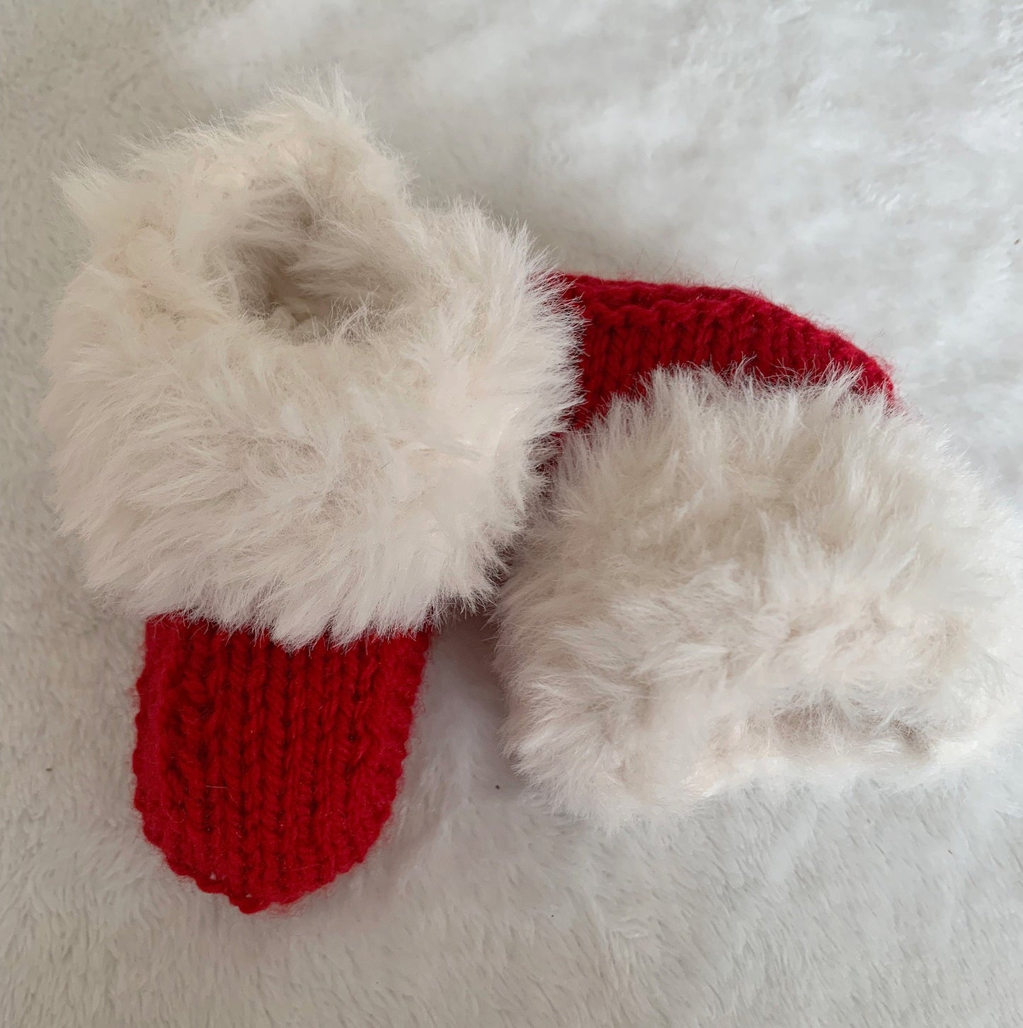 Two small red SnugaBug Christmas SnUGG Boots with white, fluffy cuffs rest on a soft white surface—perfect for gifting and now available as a special Fiver Friday Deal.