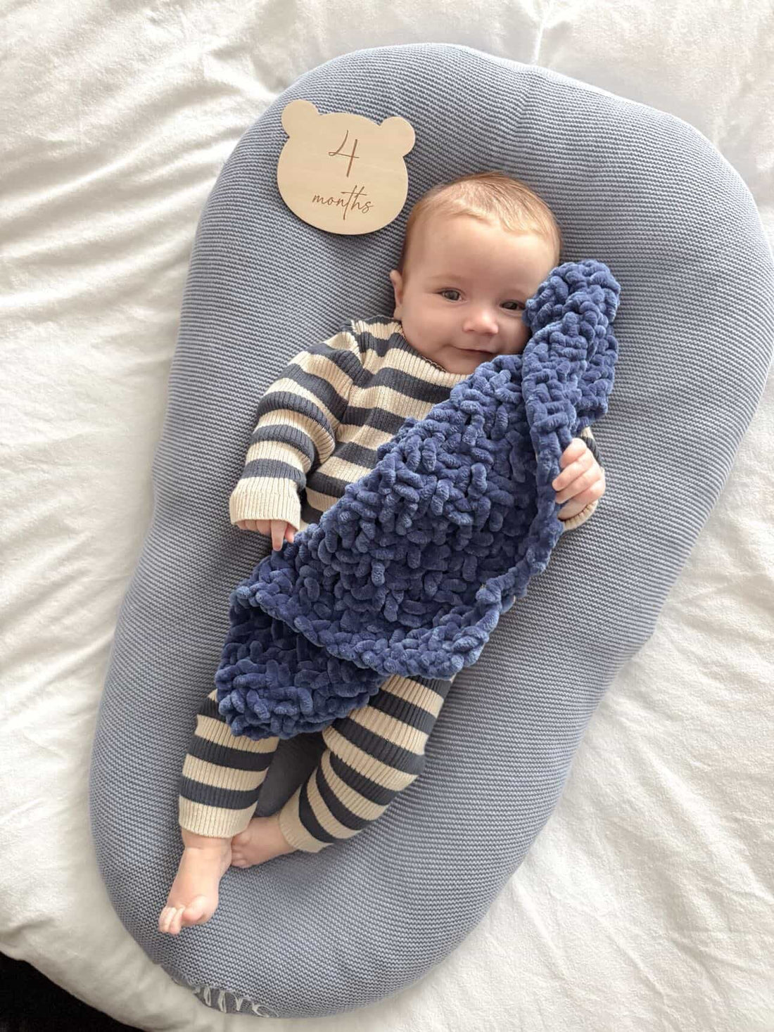 Baby holding a large hand-knitted chenille baby comforter in navy blue by SnugaBug