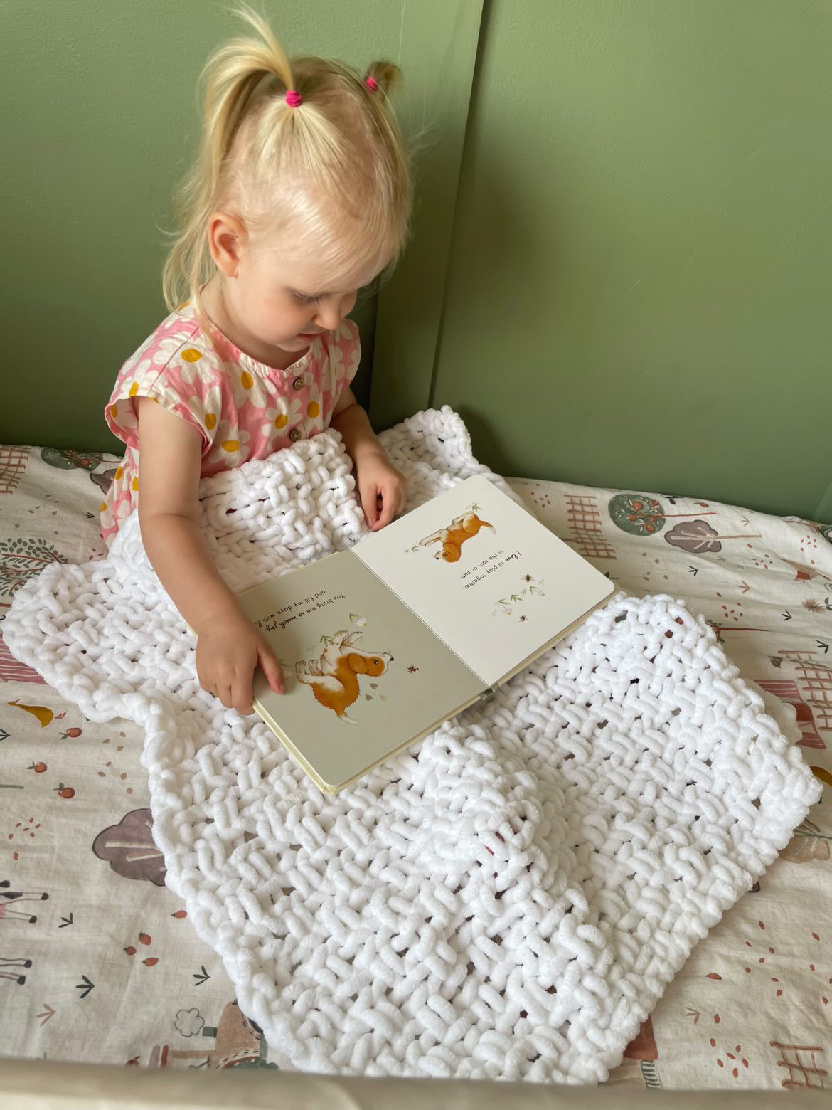 Child reading a book covered with a white knitted chenille blanket 