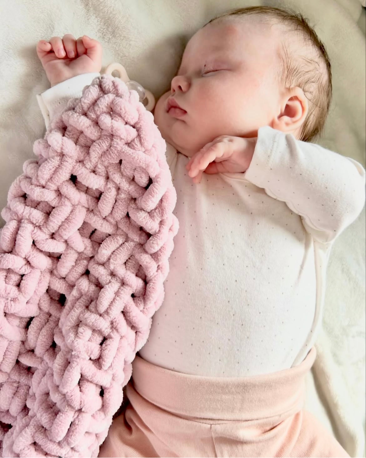 Newborn baby sleeping with a dusky pink knitted baby comforter