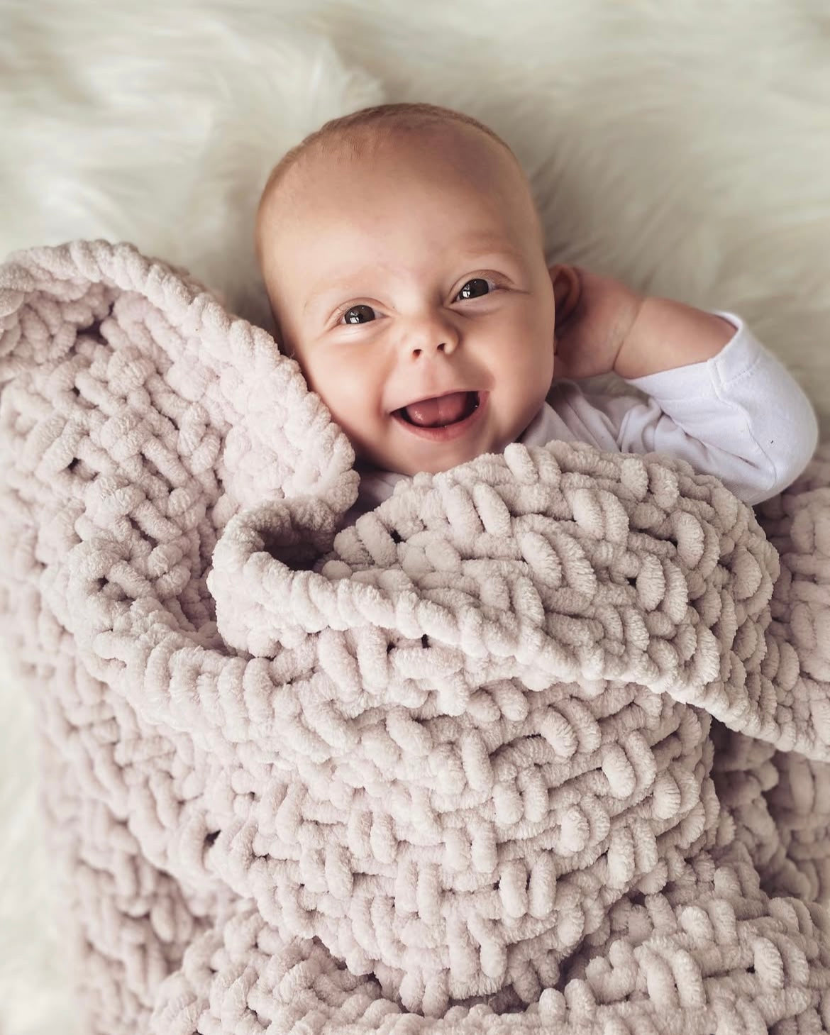 Baby wrapped in a cosy oatmeal coloured chenille baby blanket, smiling