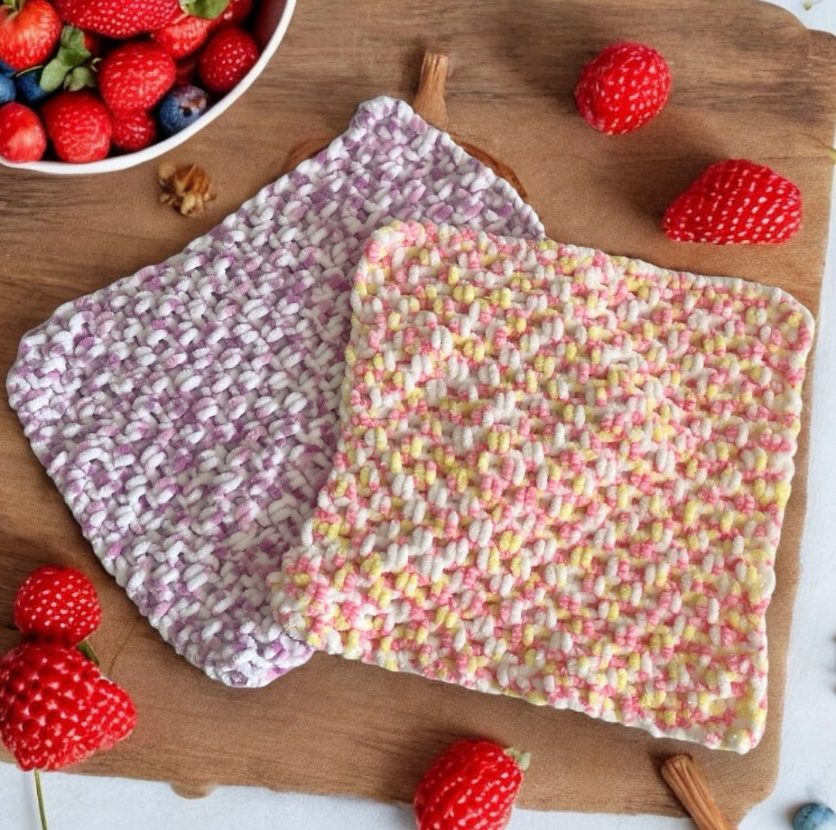 Two colourful knitted chenille baby comforters on a wooden surface with strawberries around.