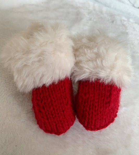 SnugaBug Christmas SnUGG Boots: small red knitted baby booties with fluffy white cuffs, Santa style, on soft white fabric—a perfect gift and part of our Fiver Friday Deal.
